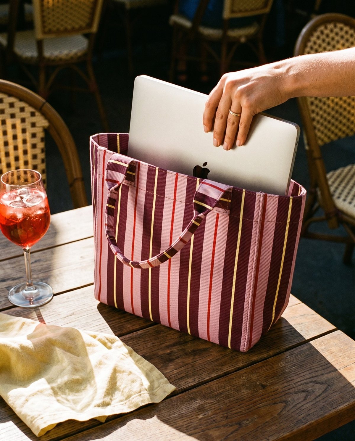 Sliding a laptop into a striped tote at a café table