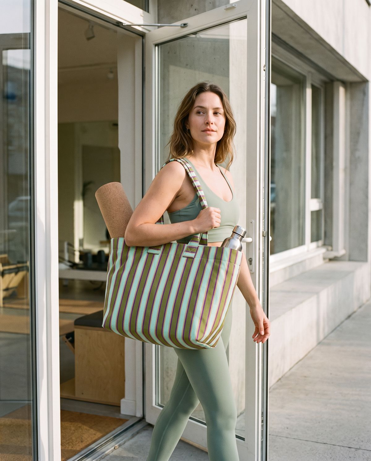 Leaving a pilates studio with a yoga mat in a striped tote